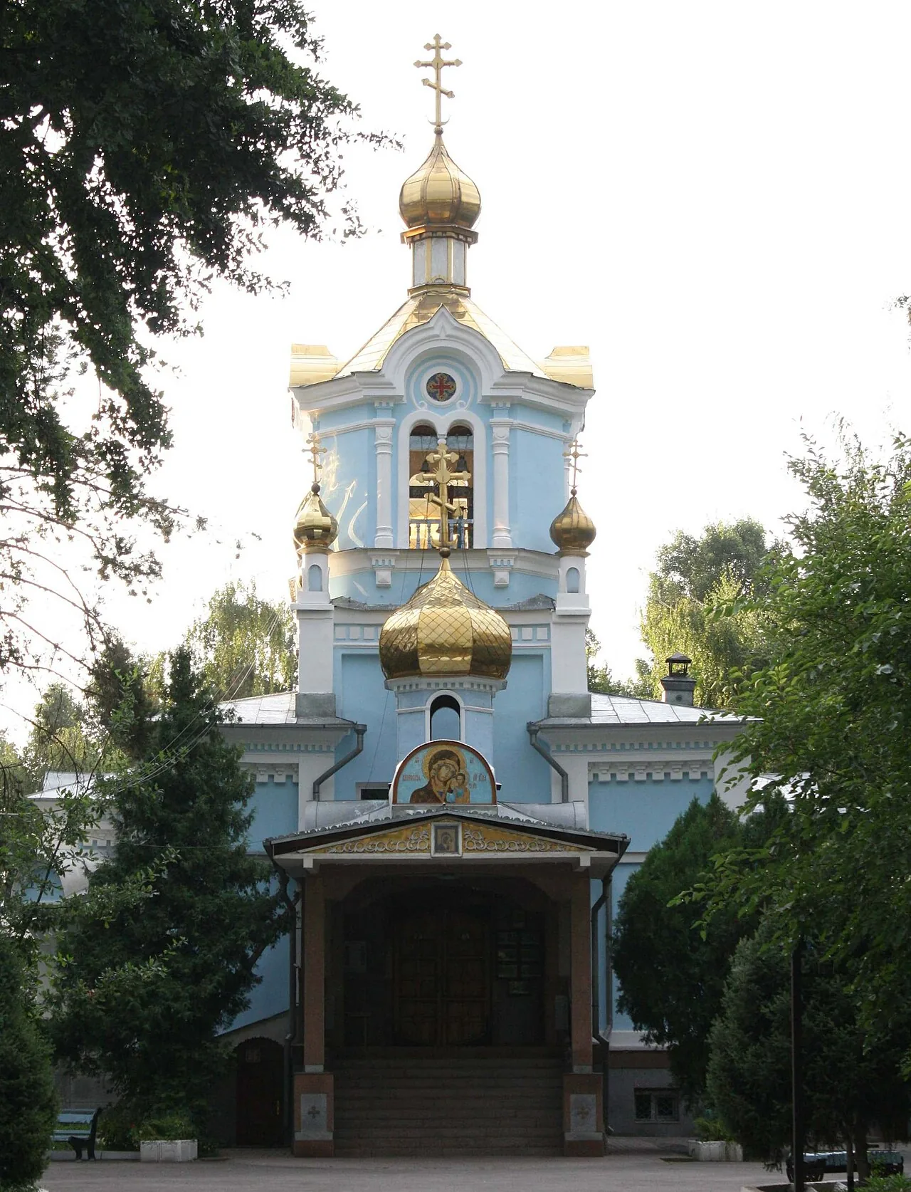 Казанский собор на Халиуллина, август 2010: голубые стены, золотые купола, кресты над шатром колокольни, крыльцо под навесом и густые деревья вокруг. Деревянный храм 1898 года, который пережил землетрясение 1911-го. Фото: Ds02006, 2010, Wikimedia Commons, общественное достояние