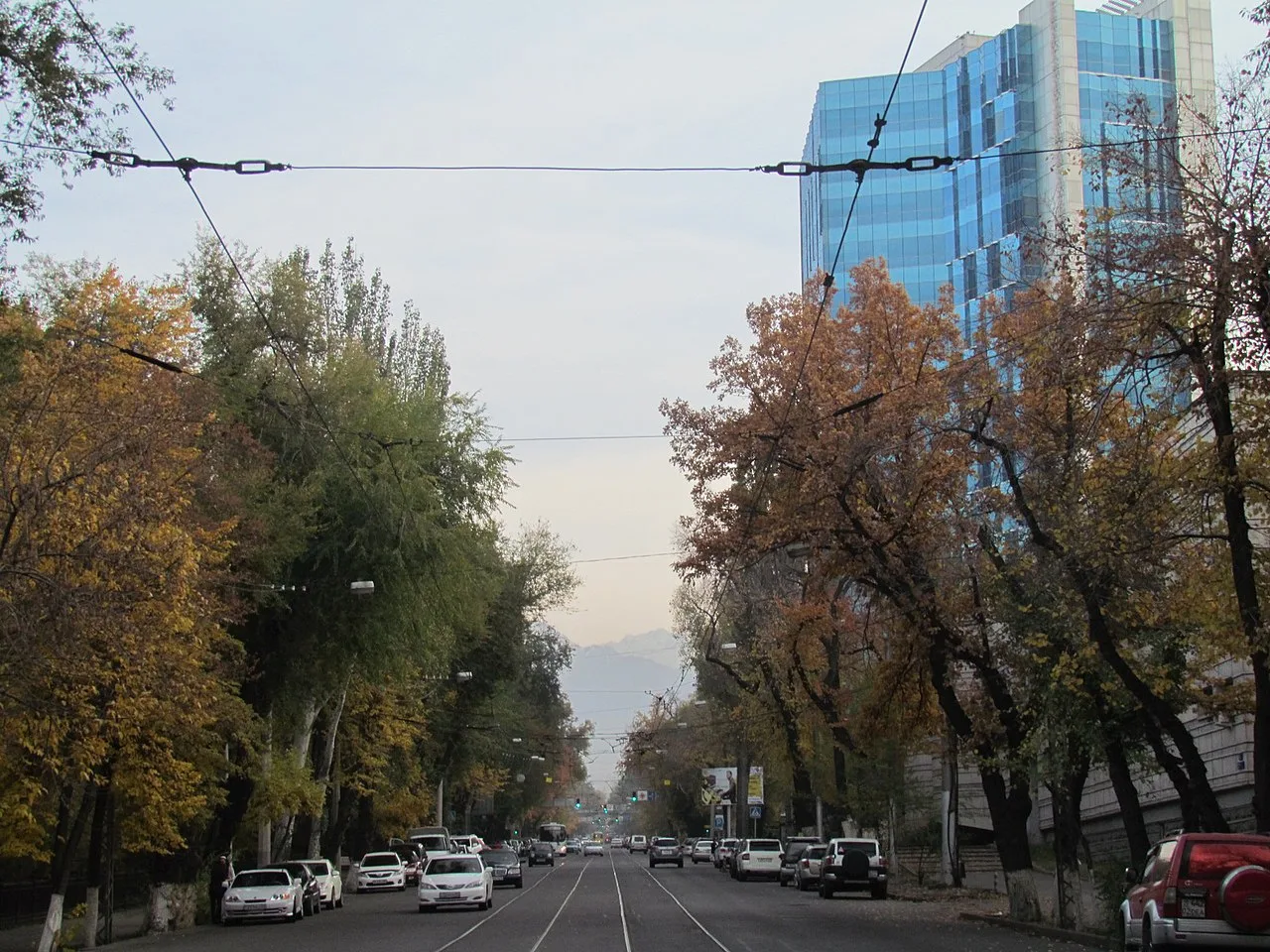 Перекрёсток Кунаева и Гоголя в октябре: жёлтые и рыжие кроны вдоль улицы, рельсы посередине, провода над дорогой, в просвете между деревьями горы. Центр, где ходят свои, осенью выглядит так, будто его тоже купили в винтаже. Фото: MarchHare1977, 2014, Wikimedia Commons, CC BY-SA 4.0