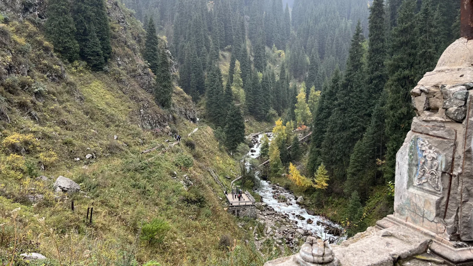 Горная река в ущелье осенью: белая вода между камнями, ели на склонах, первые жёлтые деревья у берега. Посмотрите на перекаты внизу: там, где вода белая, она громче всего. Фото: Валентин Шафранов