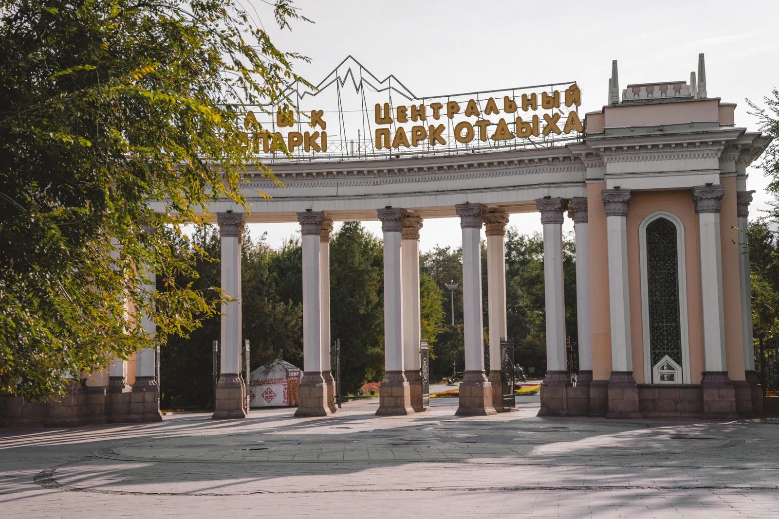 Колоннада Центрального парка осенью: белые колонны, над ними надпись по-казахски и по-русски «Центральный парк отдыха» и силуэт гор. Утром у входа пусто, и колоннаду можно снять без людей — днём такой удачи не будет. Фото: Валентин Шафранов