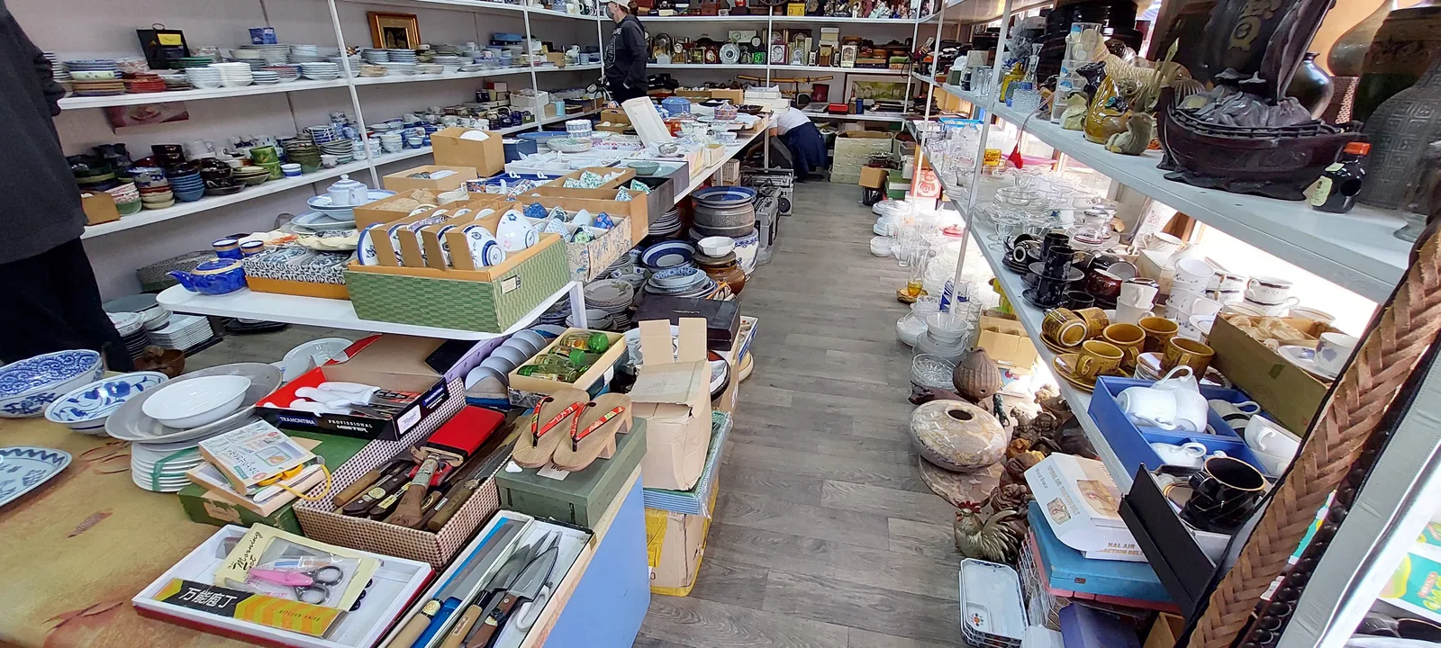 Лавка на рынке: пиалы в синих узорах, чайники, стопки тарелок до потолка, в проходе продавец разбирает коробку. Посмотрите на нижнюю полку слева — пиалу для воскресного чая выбирают здесь дольше, чем картошку на неделю. Фото: Валентин Шафранов