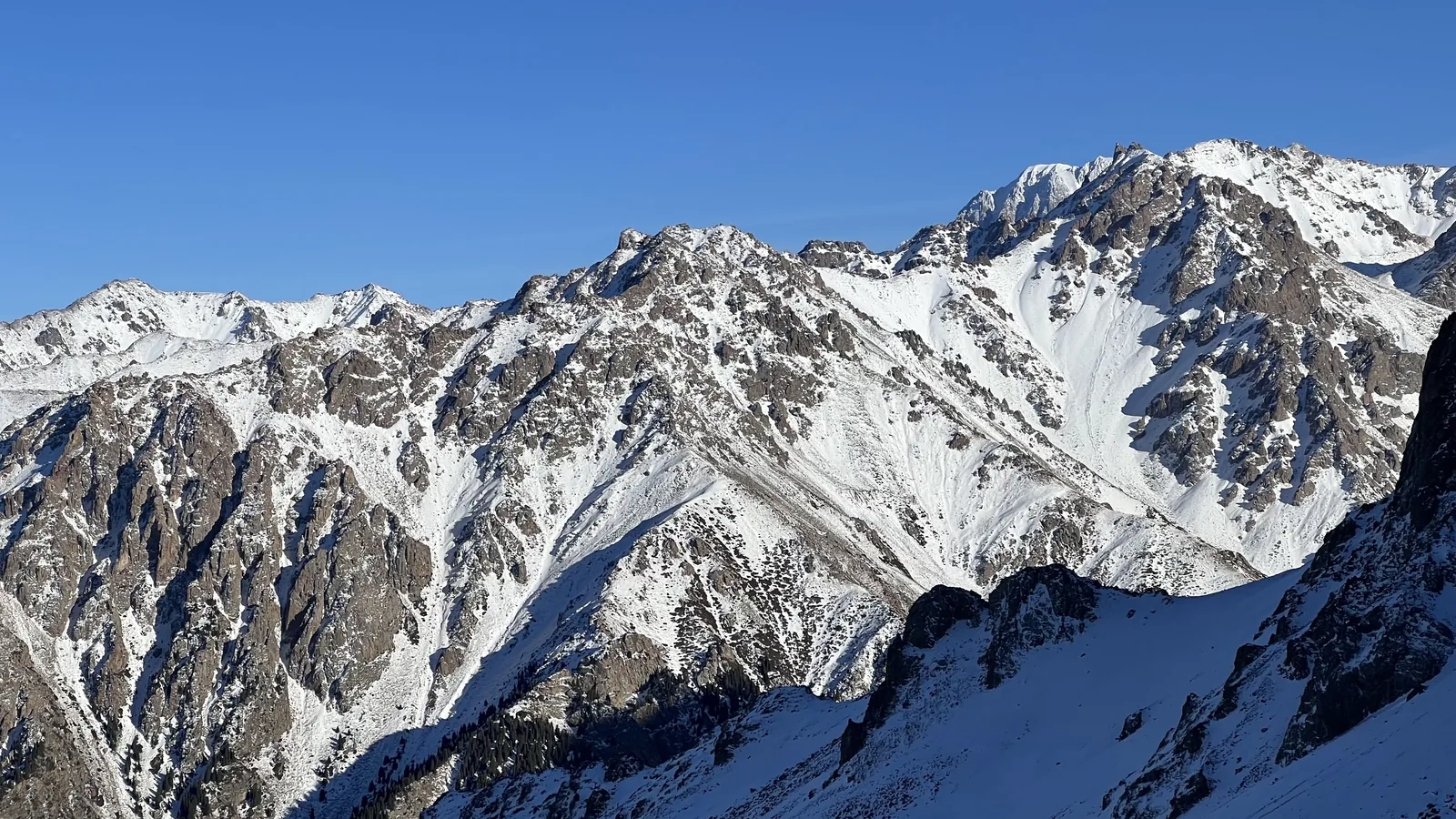Декабрь, горы над городом: снег на гребнях, камень пробивается сквозь белое, нижний склон ещё в тени. Такой вид — награда за подъём, до которого не нужны ни верёвки, ни кошки. Фото: Валентин Шафранов, декабрь 2023